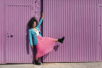 Woman holding umbrella standing against pink wall