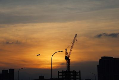 Silhouette crane at construction site against sky during sunset