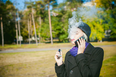 Young woman talking on mobile phone while smoking at park