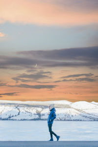 Man walking by frozen lake against sky during sunset