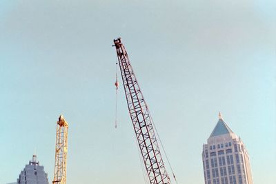 Low angle view of crane by building against sky