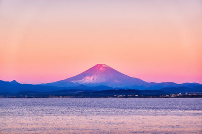 Scenic view of sea by mountains against sky during sunrise