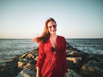 Smiling young woman standing on beach against clear sky