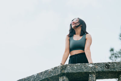 Low angle view of young woman standing against clear sky