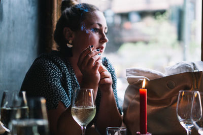 Side view of woman smoking cigarette while sitting with wineglass at restaurant table