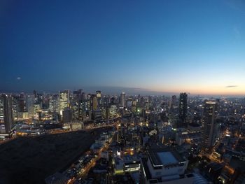 Illuminated cityscape against clear blue sky at night