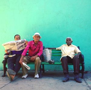 Full length portrait of friends sitting on bench against wall