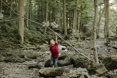 Playful boy lifting stick while standing in forest