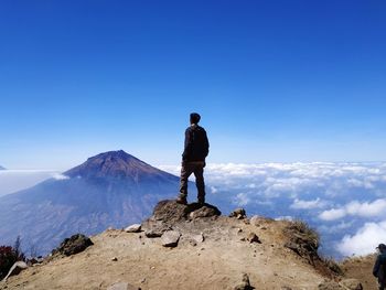 Back view of man alone standing on mountain looking up at blue blue sky