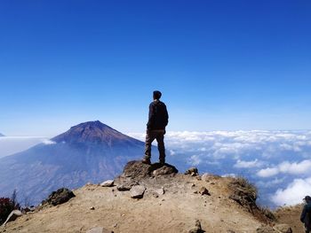 Rear view of man standing on mountain against blue sky