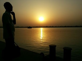 Side view of silhouette man standing by lake against sky during sunset