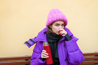 Young cute girl with dark hair in pink down jacket sits on wooden bench