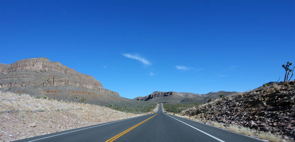 Road leading towards mountains against clear blue sky