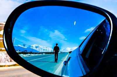 Rear view of man on road reflecting in car side-view mirror