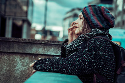 Woman in warm clothing standing by retaining wall in city