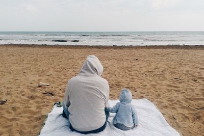 Low section of man sitting on beach against sky