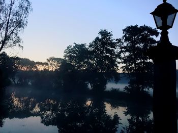 Silhouette trees by lake against sky