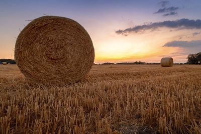 Hay bales on field against sky during sunset