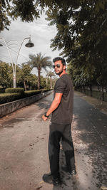 Portrait of young man standing on road against trees