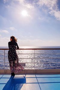 Rear view of woman standing by railing on boat deck in sea against sky