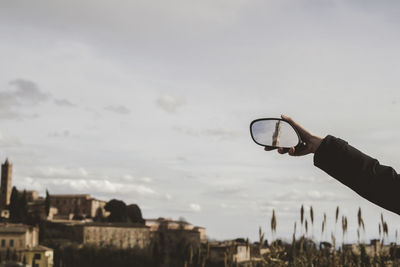 Cropped image of hand holding mirror with reflection of torre del mangia