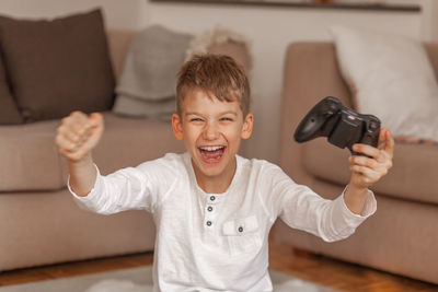 Portrait of happy boy holding video game remote control in living room at home 