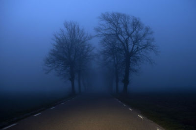 Empty road amidst trees against foggy sky