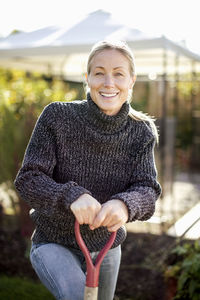 Portrait of smiling woman holding shovel at garden