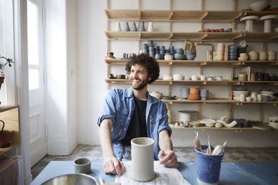 Smiling mid adult man looking away while sitting in pottery class