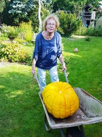 Portrait of woman pushing wheelbarrow with large pumpkin in back yard