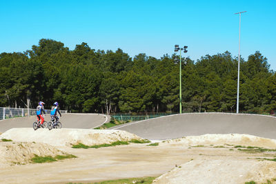 Rear view of people bmx cycling against trees