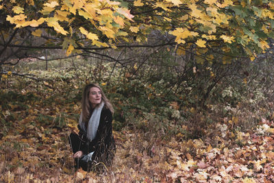 Portrait of young woman sitting on tree during autumn