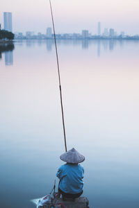 Rear view of man fishing in lake against sky