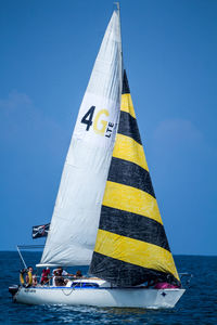 People enjoying in sailboat moving on sea against clear blue sky