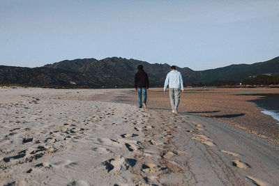 Rear view of people walking at desert against clear sky