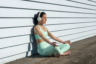 Woman meditating practicing yoga sitting in the sun wearing headphones.