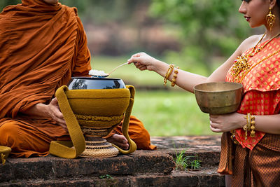 Young woman wearing traditional clothing taking cooked rice from container by monk