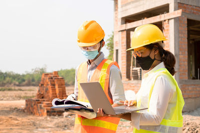 Rear view of man using digital tablet while sitting at construction site