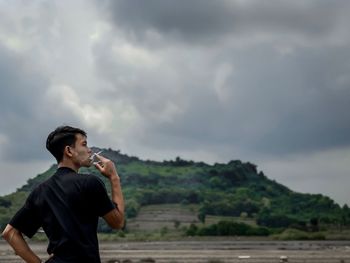 Man smoking cigarette against cloudy sky