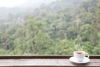 Coffee cup on table against trees