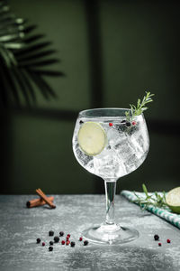 Gin tonic cocktail and shadows next to the window on dark concrete background. vertical format.