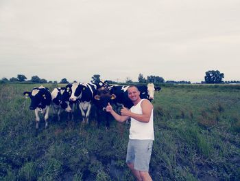 Portrait of mature man gesturing while standing by cows at farm against sky