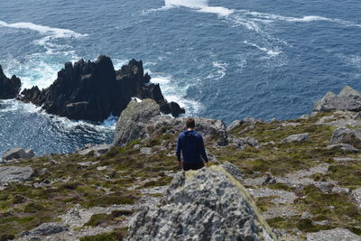 Rear view of man standing on cliff by sea against sky