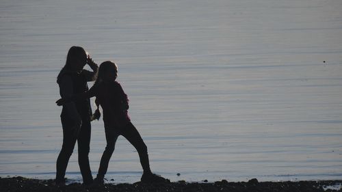 Silhouette couple standing on beach against sky