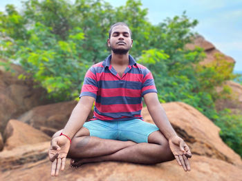 Young man doing yoga on rock