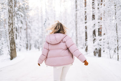 Blurred photo of young blonde woman in winter clothes walking in snowy winter forest