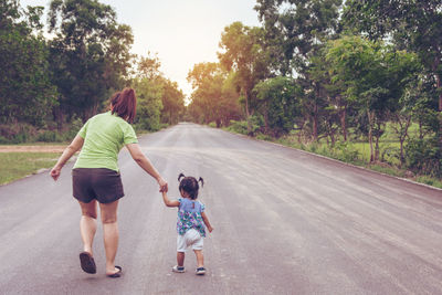 Rear view of woman with daughter walking on road amidst trees