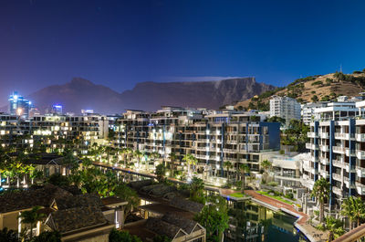 Illuminated city by mountains against sky at dusk