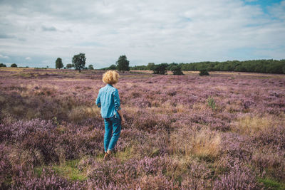 Rear view of woman walking on field against sky