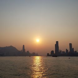 Scenic view of sea by buildings against sky during sunset